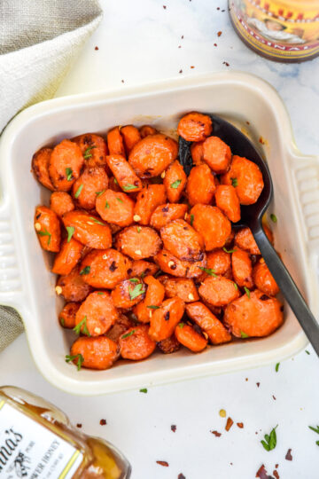 Honey-sriracha glazed carrots on a white plate with fresh herbs