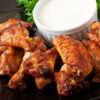 A platter of crispy baked chicken wings coated in a spicy, tangy glaze, served with celery sticks and creamy dip.