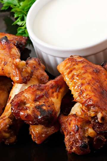 A platter of crispy baked chicken wings coated in a spicy, tangy glaze, served with celery sticks and creamy dip.