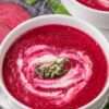 Bright magenta beet soup in a white bowl, topped with sour cream and fresh herbs.