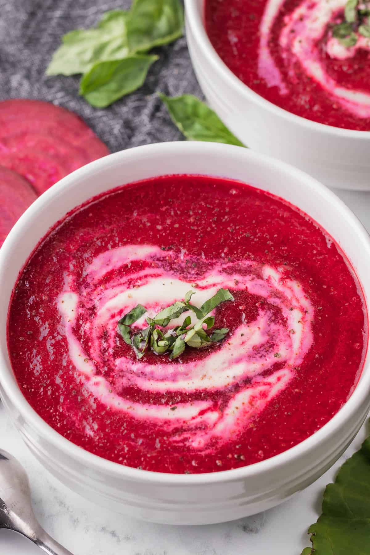 Bright magenta beet soup in a white bowl, topped with sour cream and fresh herbs.