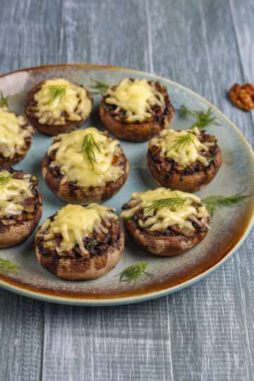 A platter of golden-brown, cheese-stuffed mushrooms garnished with fresh herbs.