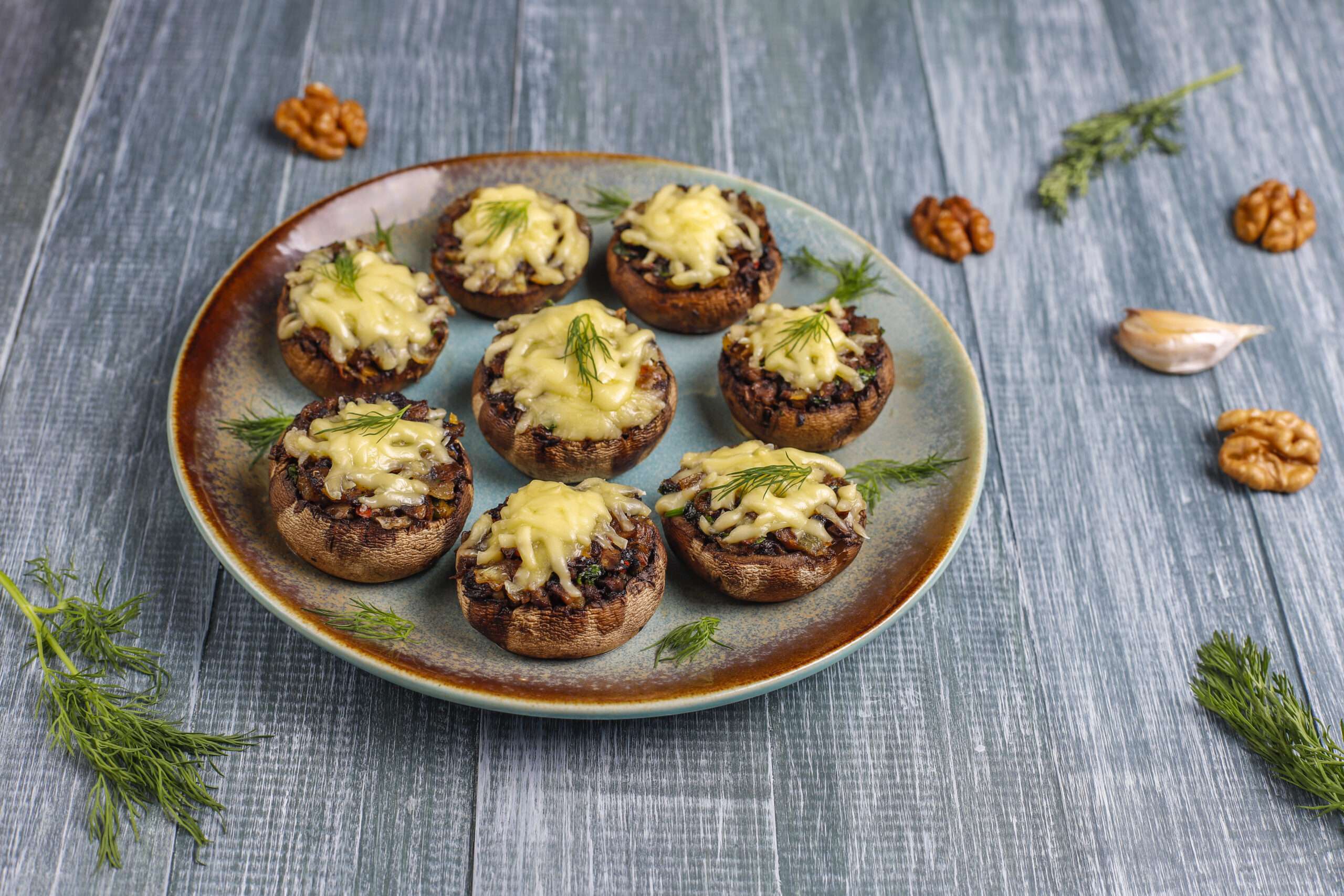 A platter of golden-brown, cheese-stuffed mushrooms garnished with fresh herbs.