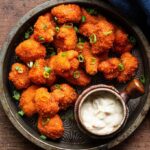 Fiery Buffalo Cauliflower Bites on a white plate garnished with celery and ranch dip.