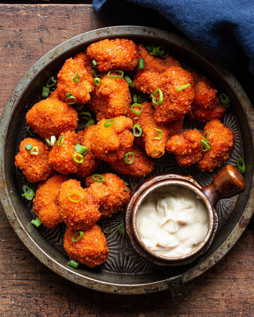 Fiery Buffalo Cauliflower Bites on a white plate garnished with celery and ranch dip.