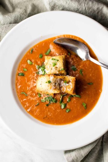 A bowl of roasted tomato basil soup topped with crispy, cheese-laden croutons.