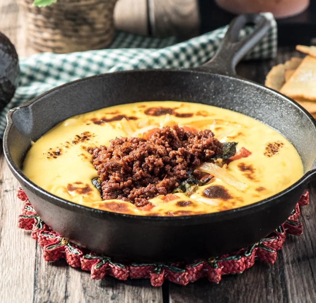 Queso Fundido with chorizo in a cast-iron skillet, topped with melted cheese and peppers.