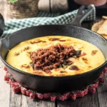 Queso Fundido with chorizo in a cast-iron skillet, topped with melted cheese and peppers.