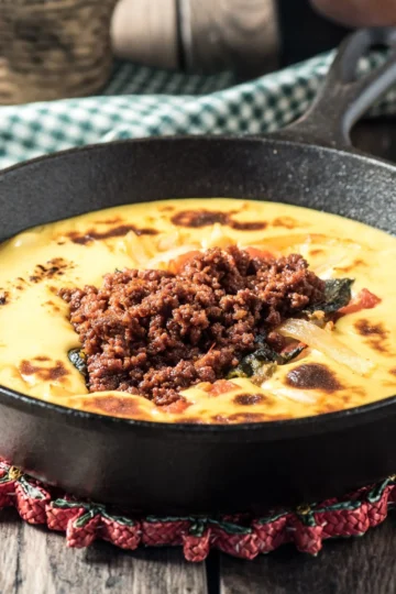 Queso Fundido with chorizo in a cast-iron skillet, topped with melted cheese and peppers.