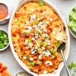 A bubbling Buffalo Chicken Dip in a casserole dish, topped with melted cheese and sliced green onions.