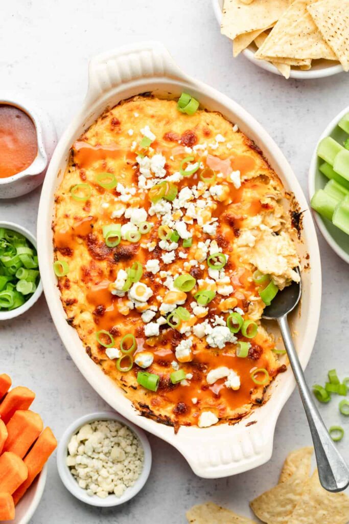 A bubbling Buffalo Chicken Dip in a casserole dish, topped with melted cheese and sliced green onions.