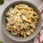 A saucepan filled with spinach alfredo pasta, sprinkled with parmesan