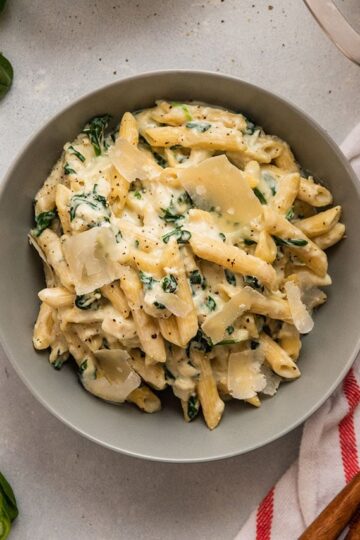 A saucepan filled with spinach alfredo pasta, sprinkled with parmesan