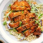 Sliced crispy chicken katsu on a plate with shredded cabbage and sauce