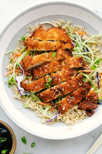 Sliced crispy chicken katsu on a plate with shredded cabbage and sauce