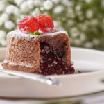 molten chocolate raspberry lava cakes with chocolate sauce pouring out, garnished with fresh raspberries.