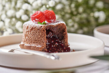 molten chocolate raspberry lava cakes with chocolate sauce pouring out, garnished with fresh raspberries.