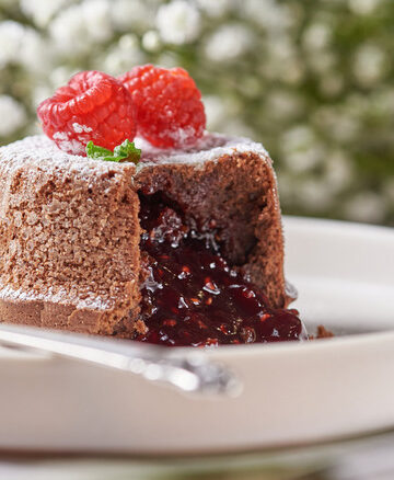 molten chocolate raspberry lava cakes with chocolate sauce pouring out, garnished with fresh raspberries.