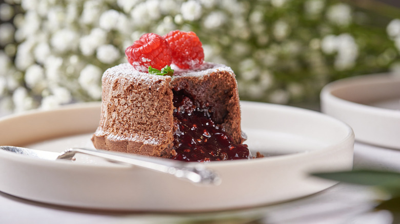 molten chocolate raspberry lava cakes with chocolate sauce pouring out, garnished with fresh raspberries.