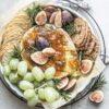 Baked Brie with Fig Jam served with assorted crackers and a sprinkle of fresh herbs