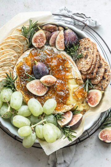 Baked Brie with Fig Jam served with assorted crackers and a sprinkle of fresh herbs