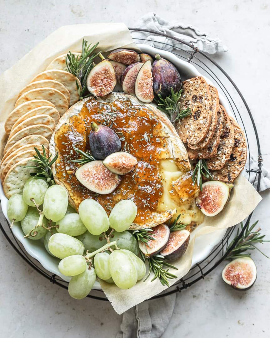 Baked Brie with Fig Jam served with assorted crackers and a sprinkle of fresh herbs