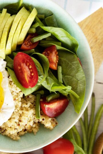 Quinoa Breakfast Bowl topped with poached eggs, fresh spinach, and a squeeze of lemon