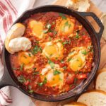 Shakshuka Recipe with vibrant tomatoes, bell peppers, and poached eggs in a rustic skillet