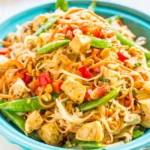 Thai Peanut Butter Chicken with Noodles topped with chopped peanuts, fresh cilantro, and lime wedges.